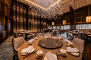 Elegant fine dining restaurant interior at Hilton Singapore with round tables, lazy susan, white porcelain settings, and dramatic floral ceiling installation