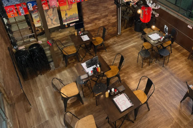 High-angle view of a casual Japanese restaurant interior with wooden floors, black metal chairs, and vintage posters