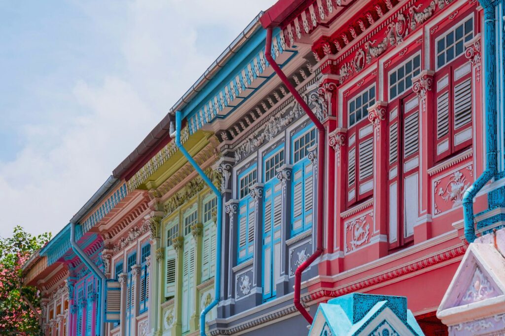 Colorful row of traditional shophouses with ornate detailing and vibrant facades in pastel shades, under a clear blue sky. Airy, cheerful atmosphere.