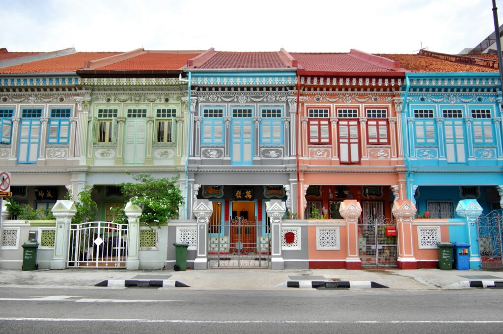Colorful row of historic shophouses with ornate details and vibrant pastel facades, in light green, blue, peach, and turquoise. A calm urban street scene.