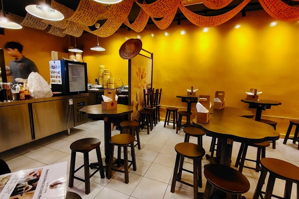 Cozy restaurant with yellow walls and wooden stools around tables; decorative hanging nets create a warm, inviting atmosphere.