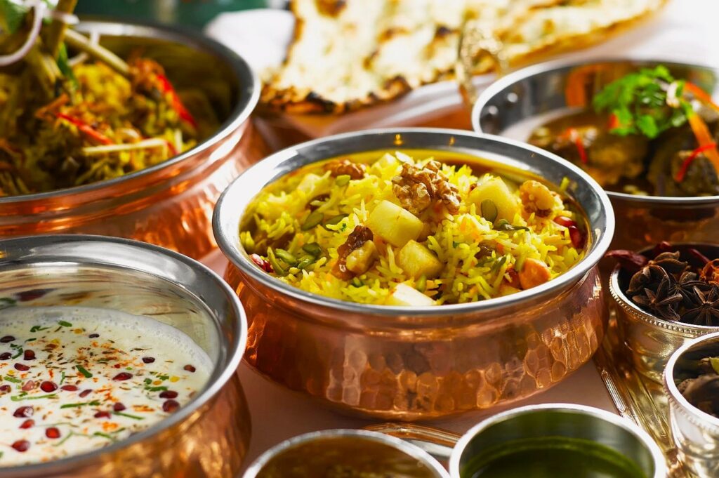 A vibrant spread of Indian cuisine in copper bowls, featuring colorful biryani, creamy raita, and naan. The scene is inviting and aromatic.