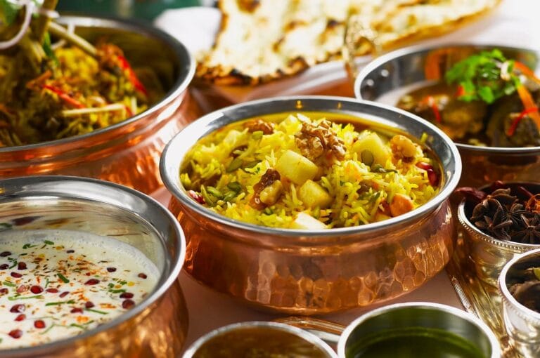 A vibrant spread of Indian cuisine in copper bowls, featuring colorful biryani, creamy raita, and naan. The scene is inviting and aromatic.