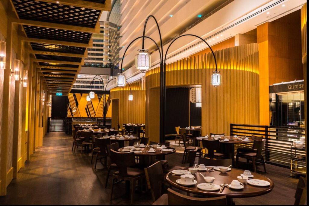 Luxurious restaurant interior with dark wooden tables set with white tableware, dim hanging lamps, and warm amber lighting, creating an elegant ambiance.
