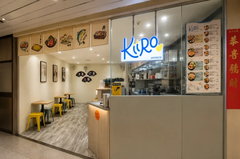 Kiiro Japanese restaurant entrance with blue neon sign, illustrated noren curtains, and yellow stools