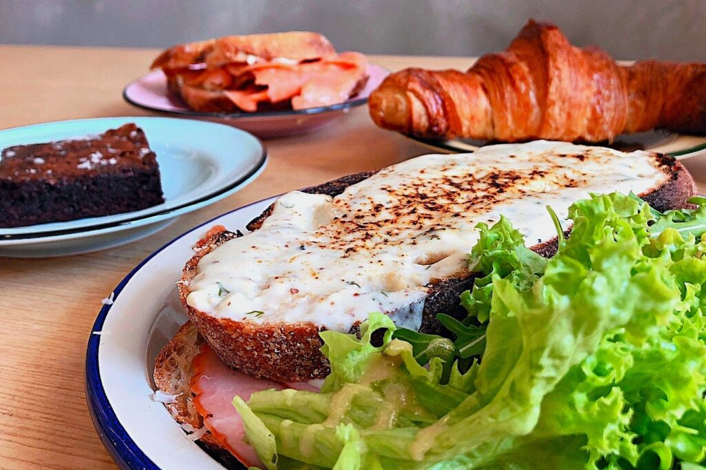 A delicious brunch spread with grilled cheese toast topped with melted cheese and lettuce, a chocolate brownie, a croissant, and a salmon sandwich.