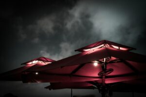 Illuminated umbrellas with soft pink light at night, set against a cloudy, moody sky. The scene feels tranquil and slightly mysterious.