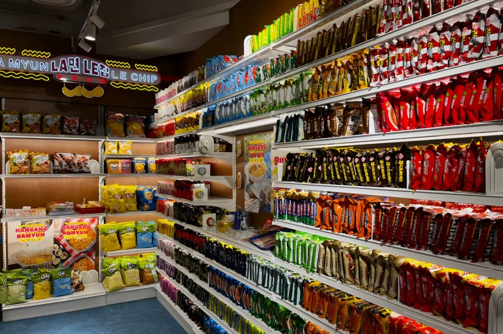 A vibrant snack aisle in a store displays neatly arranged colorful chip bags and snack packages. A neon sign above adds a playful, inviting atmosphere.