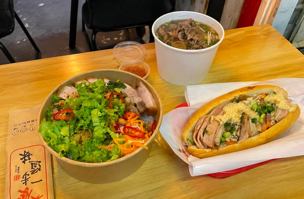 Vietnamese meal set with noodle soup, rice bowl, and baguette sandwich on a table