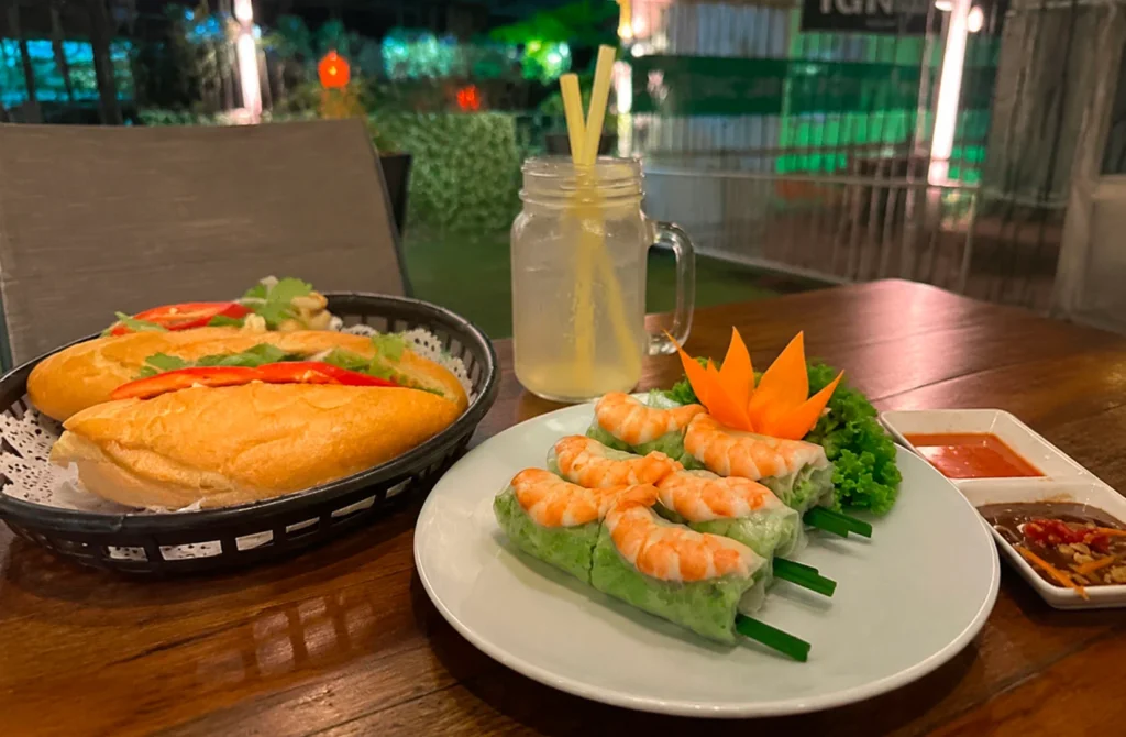 Vietnamese spring rolls and baguette sandwiches served with drinks in an outdoor dining setting
