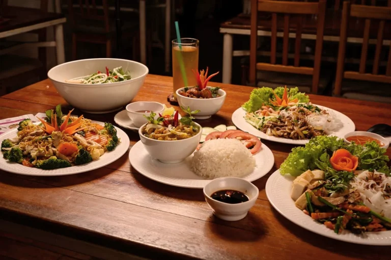 A warm-lit table displaying various Vietnamese dishes, including rice, noodles, vegetables, and garnishes, creating a welcoming and appetizing ambiance.