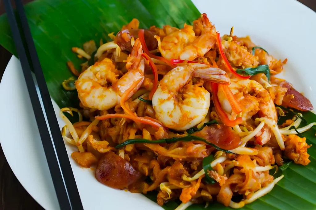 A plate of pad Thai with shrimp, noodles, bean sprouts, and vegetables on a banana leaf, accompanied by black chopsticks, creating a vibrant and appetizing look.