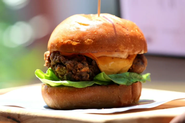 Close-up of a gourmet burger with crispy fried chicken, lettuce, cheese, and sauce in a glossy bun, set on a wooden board, emitting a hearty, indulgent vibe.