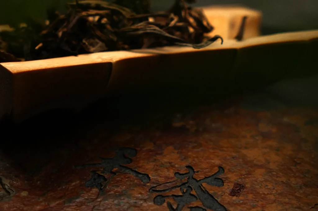 Close-up of a wooden tray with loose tea leaves, resting above a stone surface with dark engraved Chinese characters, creating a serene ambiance.