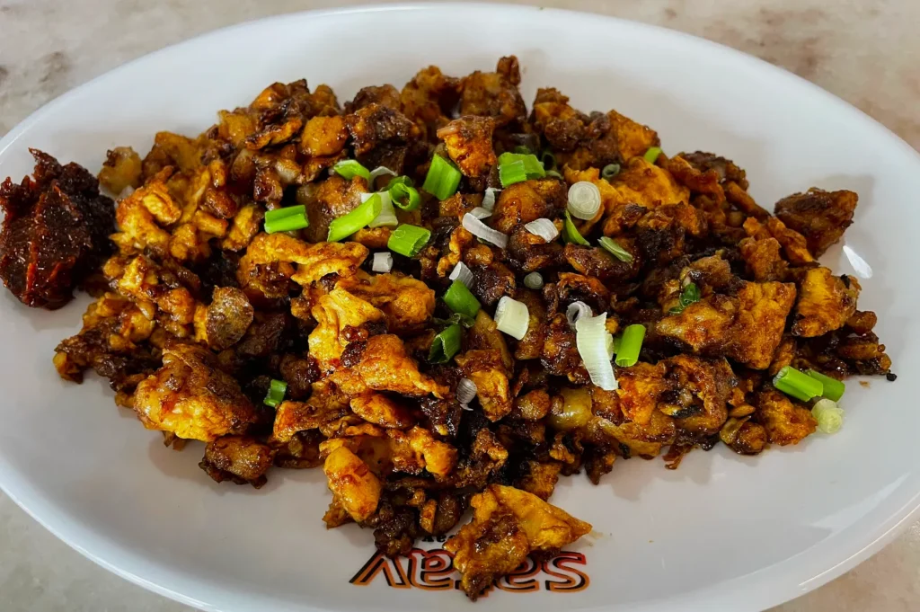 A plate of golden-brown scrambled eggs mixed with dark soy sauce and topped with chopped green onions, served with a side of spicy sambal.