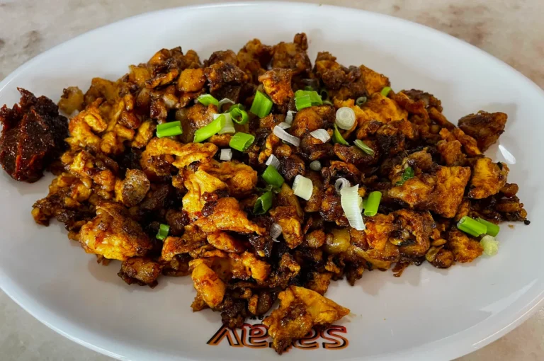 A plate of golden-brown scrambled eggs mixed with dark soy sauce and topped with chopped green onions, served with a side of spicy sambal.