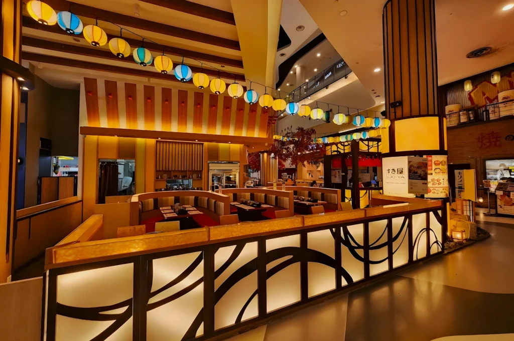 Stylish Japanese restaurant interior with warm lighting, wooden decor, and colorful lanterns, creating a cozy, inviting atmosphere. Booth seating fills the space.