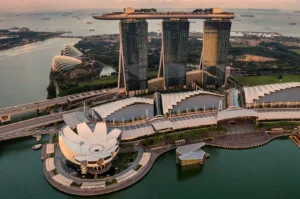 Aerial view of Marina Bay Sands in Singapore at sunset. Three towers with a ship-like rooftop and an artscience museum below, surrounded by water.
