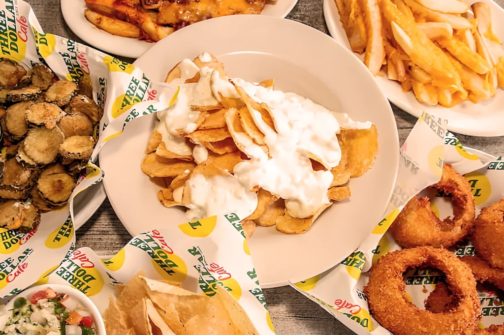 A variety of fried foods on a table including cheesy fries, onion rings, and pickles, highlighting comfort food indulgence with a casual vibe.