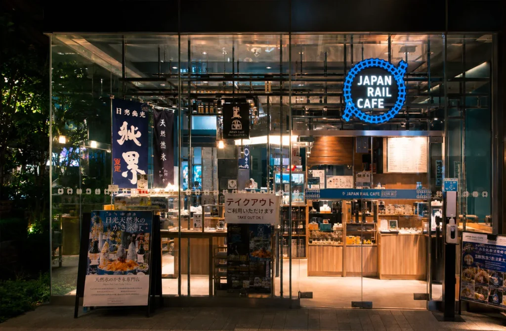 Exterior of Japan Rail Cafe with illuminated signage and glass storefront at night.