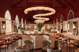 Art Deco-inspired restaurant with plush seating, round tables, and arched windows. Soft lighting and leafy plants create an elegant, inviting vibe.