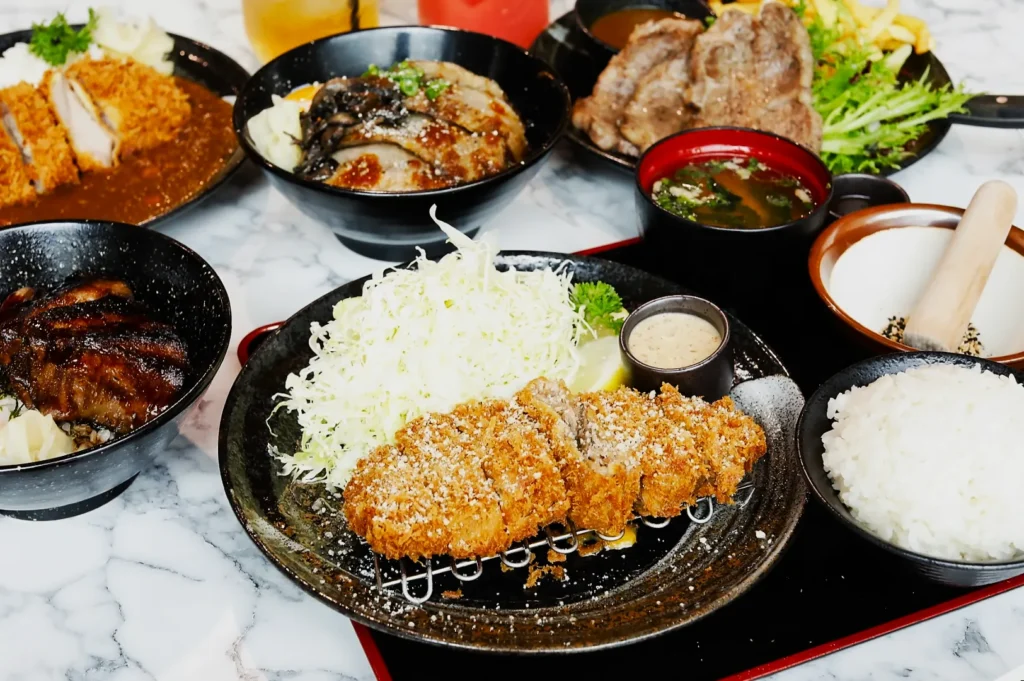 A Japanese meal on a marble table, featuring crispy tonkatsu, shredded cabbage, rice, miso soup, and garnishes, conveying a delicious, inviting scene.