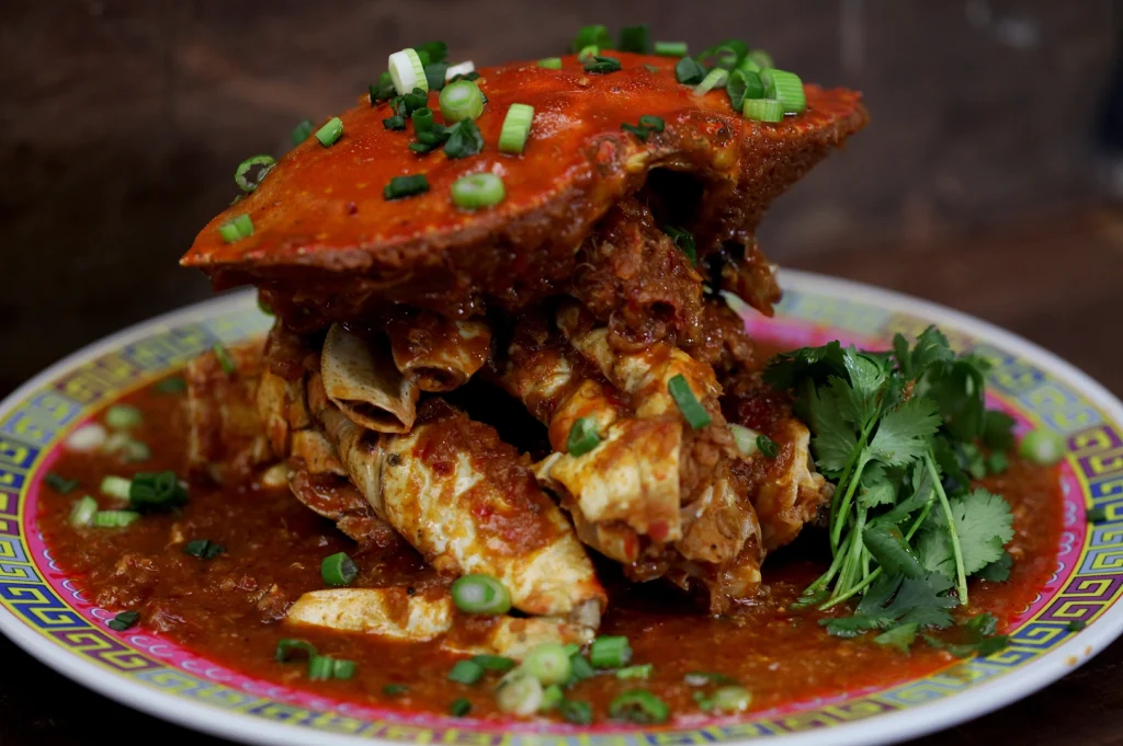 Spicy chili crab on a vibrant plate, garnished with green onions and cilantro. Rich sauce drips over the crab, creating a savory and enticing look.