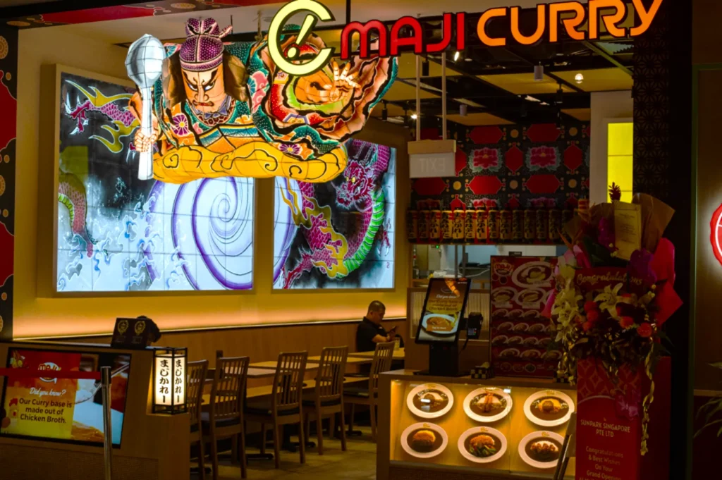 A vibrant curry restaurant features a large, colorful mural with a warrior figure. The warm interior includes display plates and floral decor, creating an inviting atmosphere.
