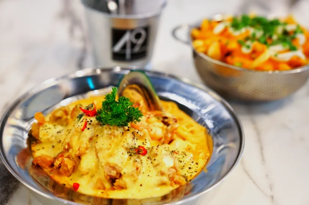 A steaming plate of creamy seafood pasta topped with parsley and red chili slices is in the foreground. A side of cheesy fries is in the background.