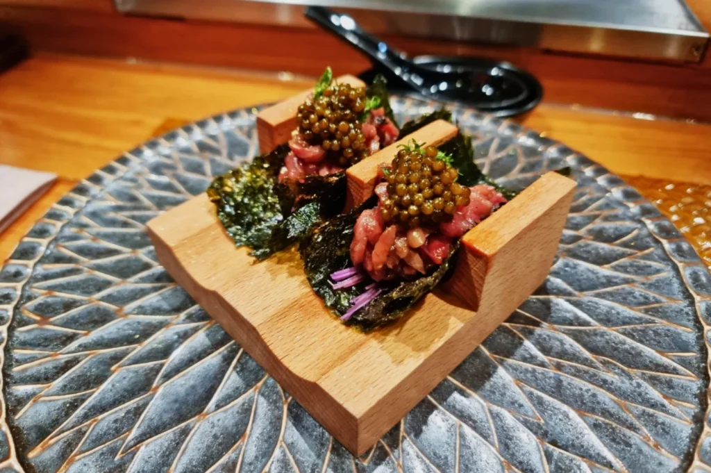 Two gourmet appetizers on a wooden stand, featuring seaweed, raw meat, and caviar, elegantly presented on a decorative plate. Luxurious and refined.