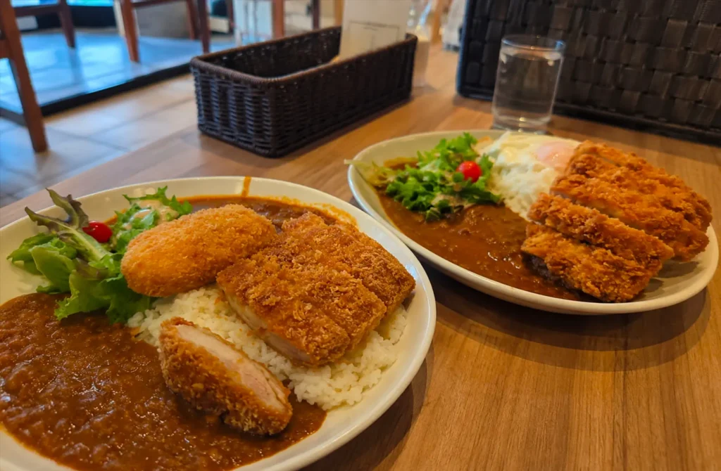 Japanese curry rice with crispy pork cutlet, croquette, salad, and fried chicken served at a restaurant table.