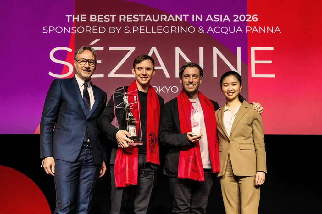 A group of four smiling individuals stands on stage. Two hold awards in front of a backdrop reading "The Best Restaurant in Asia 2026, Sézanne."