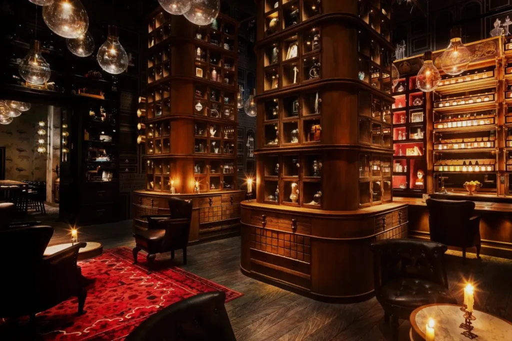 Dimly lit room with tall wooden shelves displaying various objects, creating a cozy atmosphere. Leather chairs and a red rug add warmth.