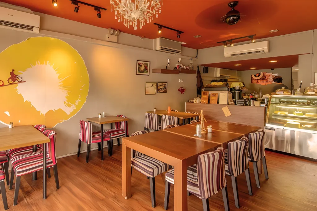 Cozy cafe with warm, orange ceiling and striped chairs. A large wall mural of a cyclist riding into the sun adds a whimsical touch.