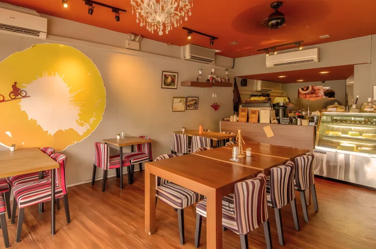 Cozy cafe with warm, orange ceiling and striped chairs. A large wall mural of a cyclist riding into the sun adds a whimsical touch.