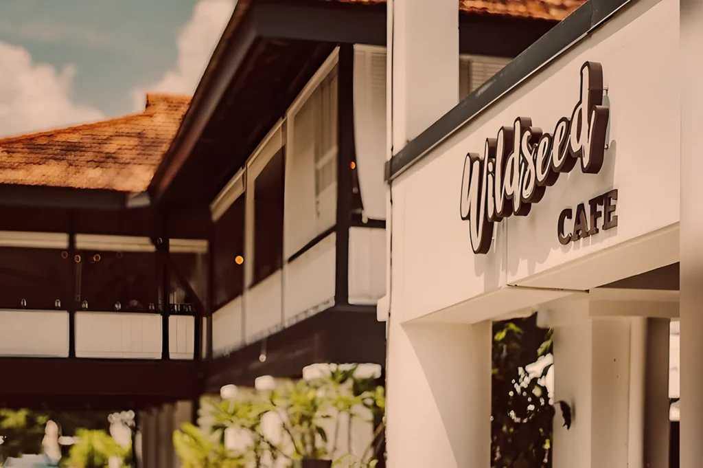 Exterior of Wildseed Café, showing its modern design with white pillars, a wooden roof, and a sign. The scene conveys a welcoming and relaxed vibe.
