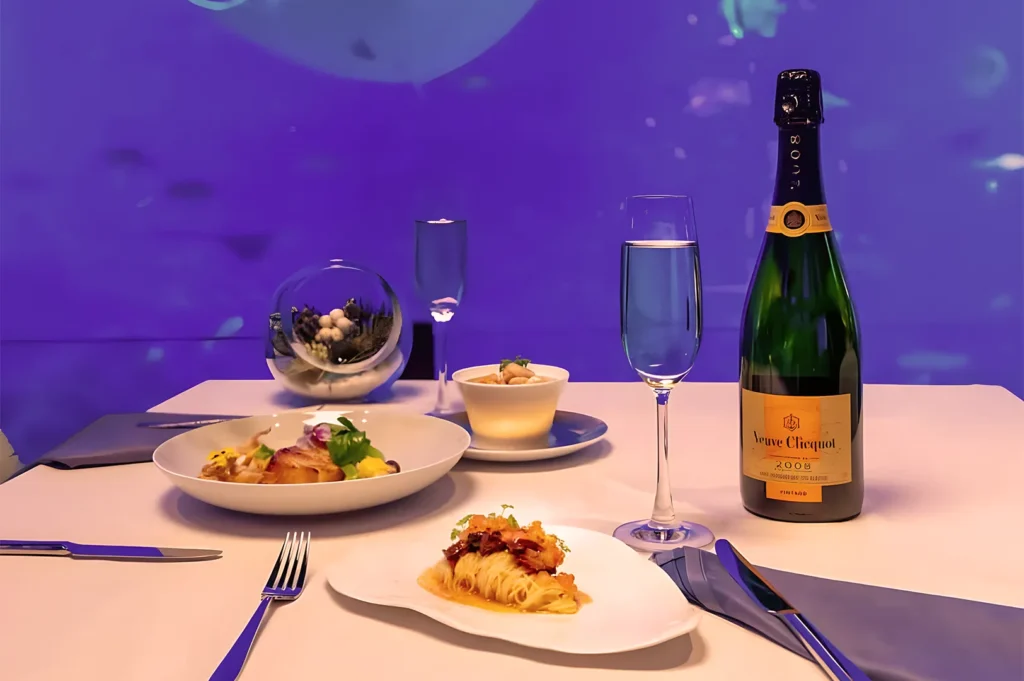 Elegant dining setup with gourmet dishes, a champagne bottle, and a flute on a white tablecloth. Background has a serene blue hue, creating a luxurious ambiance.