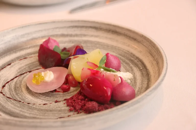 Elegant dish on a textured plate featuring colorful root vegetables, microgreens, edible flowers, and creamy elements, creating a refined and artistic presentation.