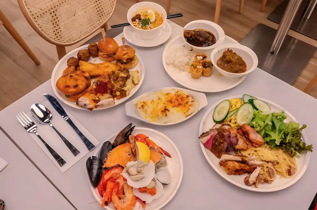 A table filled with diverse dishes, including seafood with prawns and mussels, a cheese-baked dish, pasta, fresh salad with cucumbers, rice, and curry. The setting conveys a sense of abundance and variety, perfect for a buffet.