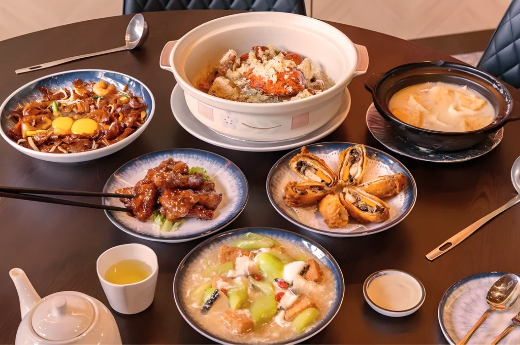 A table with a variety of Asian dishes, including a seafood pot, fried rolls, braised meat, and soups, conveying a sense of warmth and abundance.