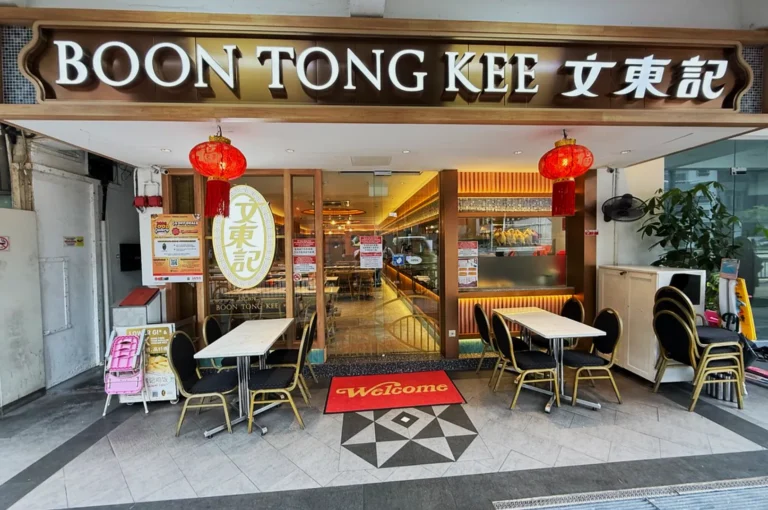 Street view of Boon Tong Kee restaurant with red lanterns and a welcoming ambiance. Outdoor seating includes tables and chairs under a sign.