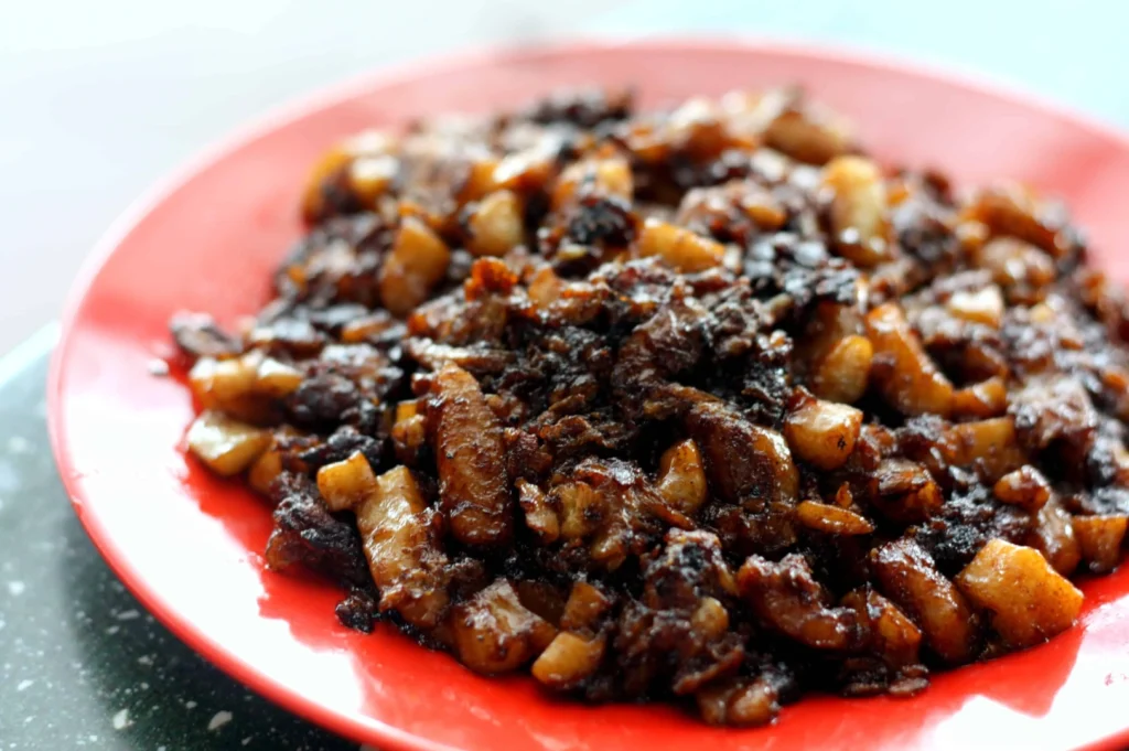 Close-up of a red plate filled with crispy, caramelized diced meat. The rich, dark glaze suggests a savory, flavorful dish.