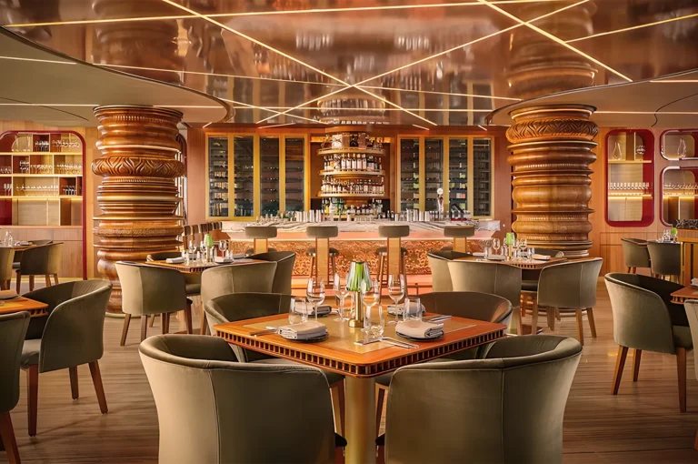 Luxurious restaurant interior with warm lighting, featuring wooden columns, elegantly set tables, plush green chairs, and a stocked bar in the background.