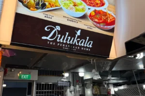 Exterior signboard of Dulukala The Peranakan Home restaurant featuring popular dishes like Chap Chye and Assam Fish Head.
