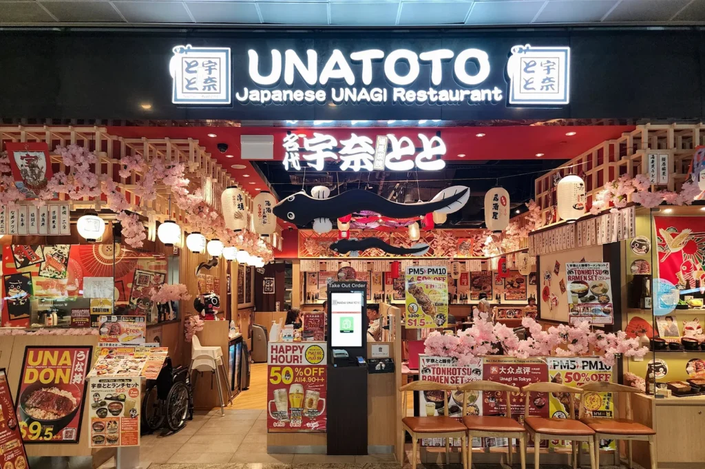 Brightly lit exterior storefront of Unatoto Japanese Unagi Restaurant featuring traditional lanterns, cherry blossom decor, and promotional menu signs at the entrance.