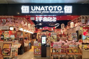Brightly lit exterior storefront of Unatoto Japanese Unagi Restaurant featuring traditional lanterns, cherry blossom decor, and promotional menu signs at the entrance.