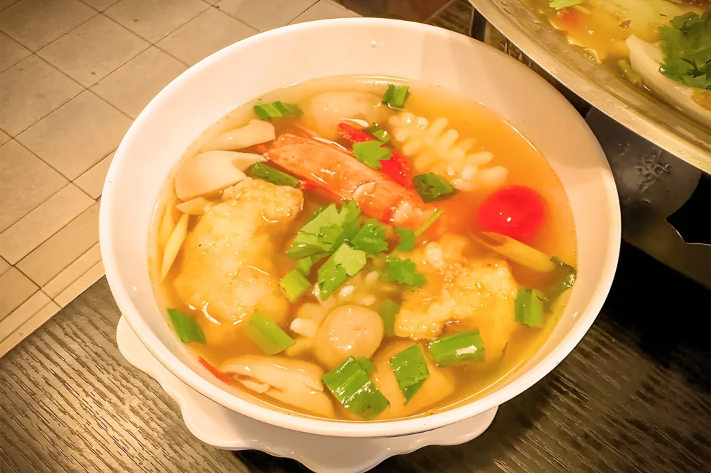A bowl of authentic Thai Tom Yum Seafood Soup from Nakhon Kitchen, featuring fresh prawns, squid, mushrooms, and fragrant herbs in a clear spicy broth.