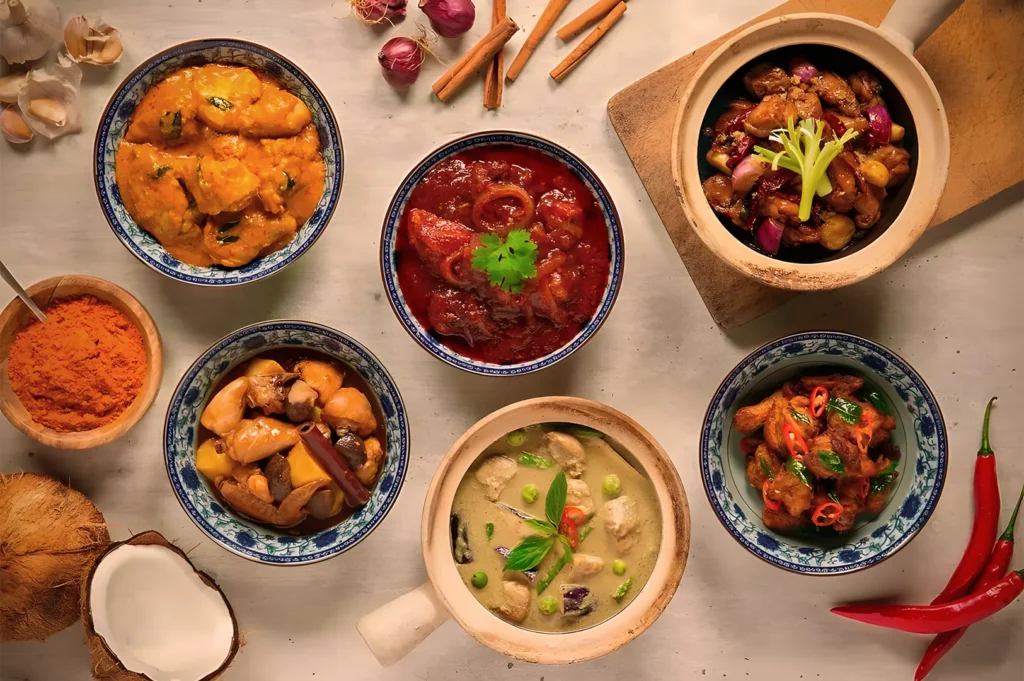 A variety of colorful curries in bowls arranged on a table, surrounded by fresh spices and herbs, conveying a sense of warmth and aromatic richness.