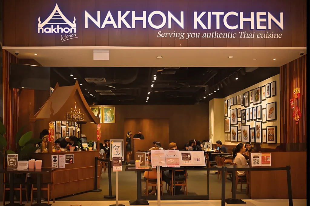 Exterior storefront of Nakhon Kitchen, a popular Thai restaurant in Singapore, showcasing its warm wooden interior and wall of framed food photography.