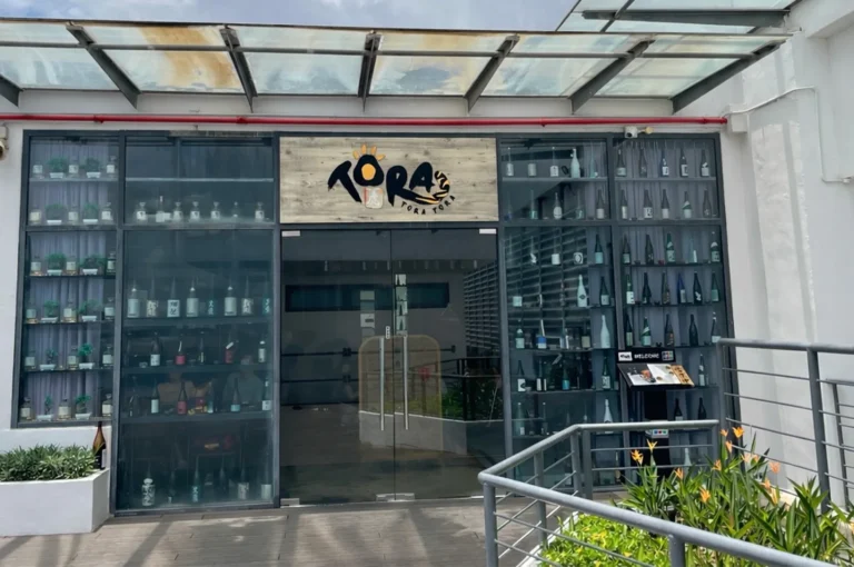 Exterior storefront of Tora Tora Japanese restaurant featuring a large glass display wall filled with various sake bottles and a modern glass awning.